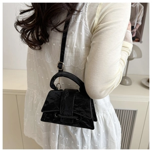 Detail of black mini crossbody bag with textured finish on a white ruffled outfit