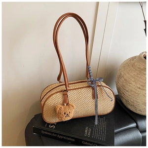 Detail of straw woven handbag with brown leather trim and cute bear charm on a book