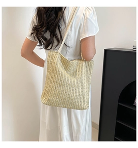 Detail of a beige woven straw tote bag shown on a model in a white dress