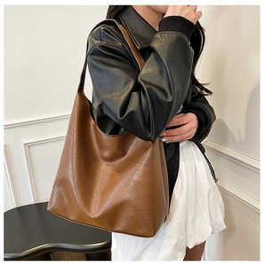 Brown leather tote bag styled on shoulder with black jacket and white skirt outfit