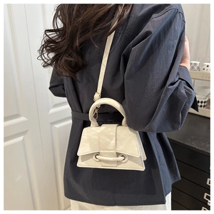 Detail of off-white mini crossbody bag featuring pleated faux leather texture and top handle