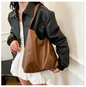 Detail of a large vintage brown tote bag worn on shoulder over a black leather jacket