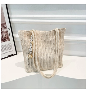 Detailed close-up of beige woven tote bag with vertical knitting and bell charm decoration