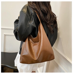 Brown leather oversized hobo bag on model's shoulder showing large capacity and texture
