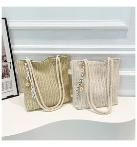 Close-up of straw tote bag with braided handles, silk scarf detail and golden ball charm