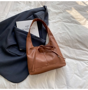 Detail of caramel brown leather tote bag with a small bow and heart-shaped metal pendant