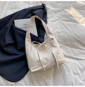 Detailed close-up of cream bow-knot tote bag with heart logo on grey blazer