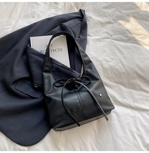 Detail of minimalist black faux leather tote featuring a subtle bow and heart metal logo