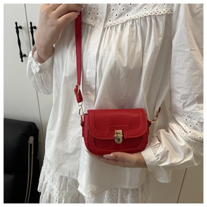 Detail of red litchi texture PU leather saddle bag with gold metal clasp on a model