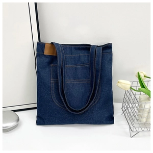 Detail of dark blue denim tote bag with brown PU leather patch and orange contrast stitching
