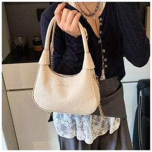 Detail of beige crescent bag featuring woven texture and gold chain decoration