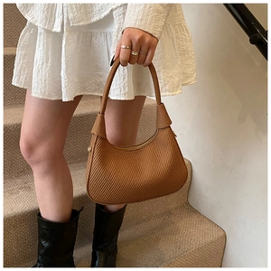 Close-up of brown woven underarm bag featuring intricate checkerboard pattern and knot detail