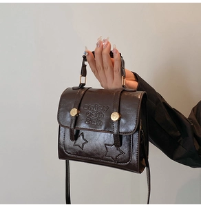 Detail of dark brown leather handbag with star embossing and gold circular metal buckle