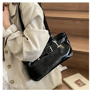 Detail of black glossy shoulder bag with silver buckle worn with a beige blazer