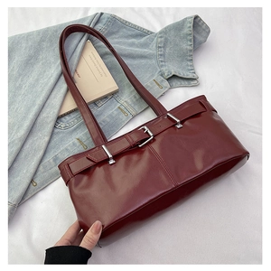 Close-up of deep red glossy leather shoulder bag with silver buckle on denim backdrop