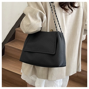 Détail d'un sac bandoulière noir avec chaîne argentée porté sur une tenue chic