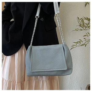 Détail du sac bandoulière bleu clair texturé avec chaîne en métal et rabat tissé