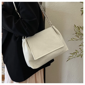 Détail d'un sac porté épaule beige texturé avec chaîne en métal argenté sur un modèle