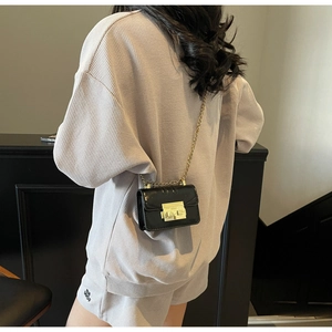 Close-up of a mini black patent leather crossbody bag with a golden chain strap and lock