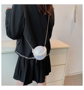 Detail of spherical evening bag with silver sequins and white chain on black dress
