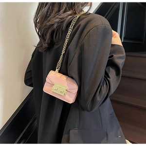 Detail of pink mini square chain bag with gold lock and glossy finish on model