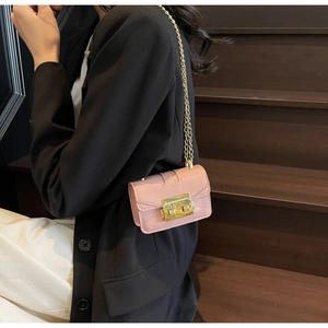 Detail of pink patent leather mini crossbody bag with gold chain strap on a model