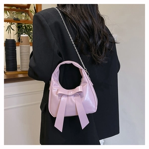 Pink bow handbag with shiny patent leather finish and silver chain strap on model