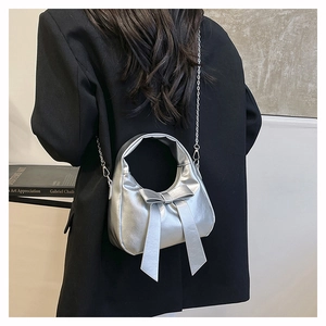 Detail of silver metallic handbag with bow accent and chain strap worn on black blazer
