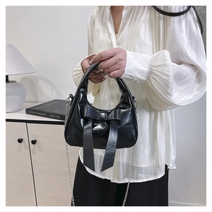 Close-up of black patent leather handbag featuring a glossy bow and silver chain strap