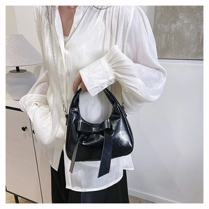 Detail of black glossy bow handbag with silver metal chain on white chiffon outfit