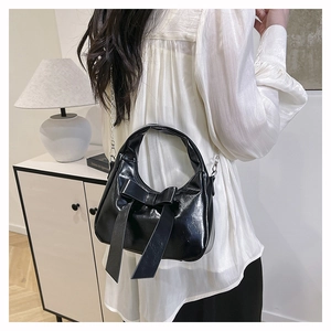 Rear view of a model wearing the black glossy patent leather bow handbag with chain strap