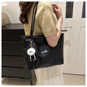Detail der schwarzen Houndstooth-Tasche mit Modetag und Plüsch-Anhänger am Modell