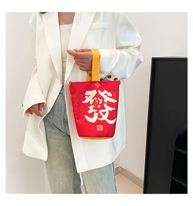 Detail of red canvas bucket bag featuring white calligraphy and yellow woven handle