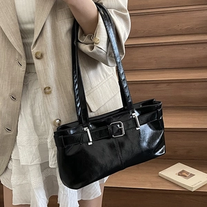 Glossy black patent leather tote bag with buckle detail shown in a chic lifestyle setting