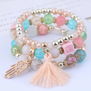 Close-up of bohemian multilayer bead bracelets with pink tassels and golden Hamsa Hand charms