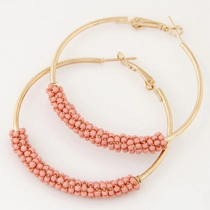 Golden metal hoop earrings with pink seed bead weaving decoration on white background