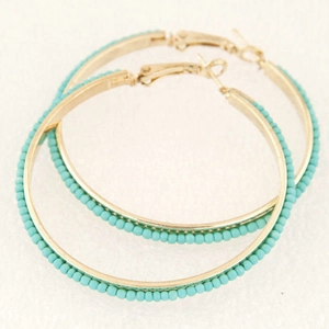 Minimalist gold hoop earrings with turquoise beaded trim against a white textured background