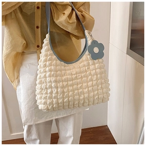Détail d'un sac hobo beige à texture popcorn avec bandoulière bleue et breloque fleur