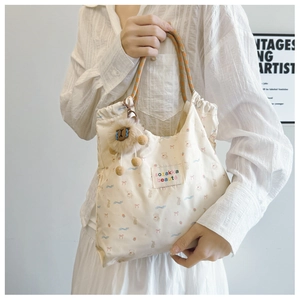 Detail of floral canvas tote bag featuring woven rope handles and a plush bear charm