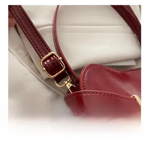 Detail der goldenen verstellbaren Schnalle an der roten Lackleder-Handtasche mit Nähten