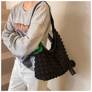 Détail du sac cabas texturé noir avec breloque fleur verte porté à l'épaule du mannequin