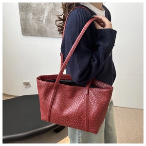 Close-up of deep red woven leather tote bag featuring a minimalist texture and shoulder straps