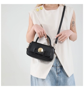 Detail of a black square bag featuring a round gold buckle and slim leather strap