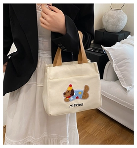 Détail du sac cabas en toile avec chien brodé et anses en ruban marron élégantes
