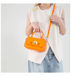 Orange leather handbag with gold metal buckle shown on model in a stylish casual outfit
