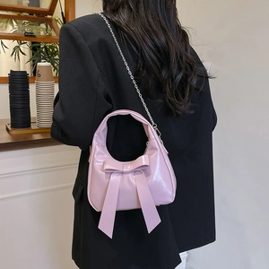 Pink bow handbag in glossy patent leather with silver chain strap shown on a model