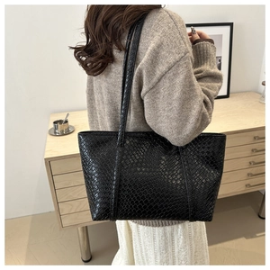 Dettaglio della borsa tote nera intrecciata con trama particolare indossata da modella