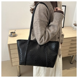 Dettaglio della borsa tote nera a trama intrecciata indossata a spalla in un interno