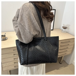 Dettaglio della borsa tote in pelle nera con trama intrecciata indossata come borsa a spalla