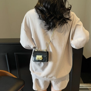 Mini black crossbody bag with gold chain strap and square metal lock on light beige outfit
